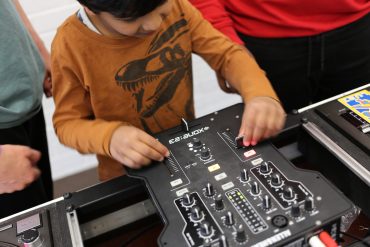 Das Bild zeigt ein Kind, das die Regler an einem Mischpult bedient.