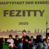 Kinder stehen auf der Bühne: Die Kinderregierung stellt sich vor - auf der FEZitty-Eröffnung am 30. Juli 2025. Hinter den Kindern ist das FEZitty-Stadtzeichen zu sehen. Es zeigt die Skyline Berlins auf gelbem Grund. Darauf geschrieben steht: "Hauptstadt der Kinder FEZitty 2025".