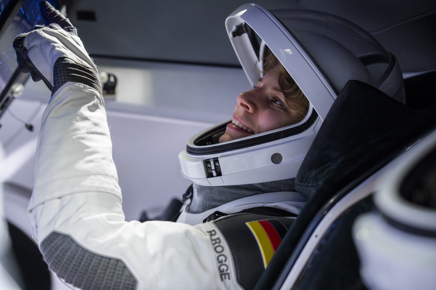 Astronautin Rabea Rogge bedient eine Konsole und trägt einen weißen Helm und Raumanzug. An die Schulter des Anzugs ist die deutsche Flagge genäht.