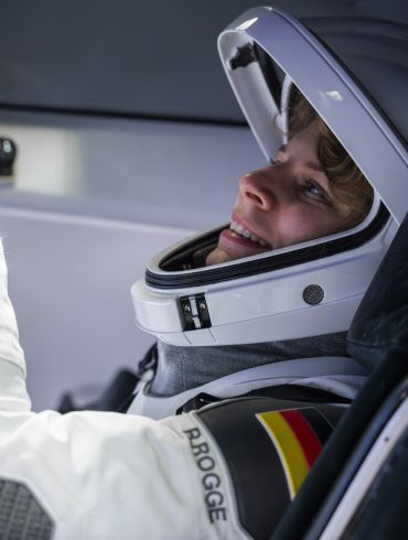 Astronautin Rabea Rogge bedient eine Konsole und trägt einen weißen Helm und Raumanzug. An die Schulter des Anzugs ist die deutsche Flagge genäht.