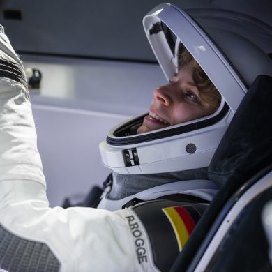 Astronautin Rabea Rogge bedient eine Konsole und trägt einen weißen Helm und Raumanzug. An die Schulter des Anzugs ist die deutsche Flagge genäht.