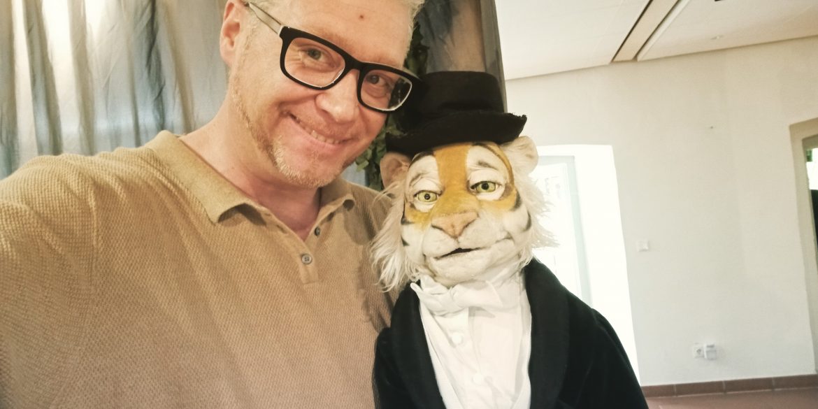 Der künstlerische Leiter des 29. Puppentheaterfests, Stefan Maatz, mit einer Tigerpuppe, die Frack und Zylinder trägt.