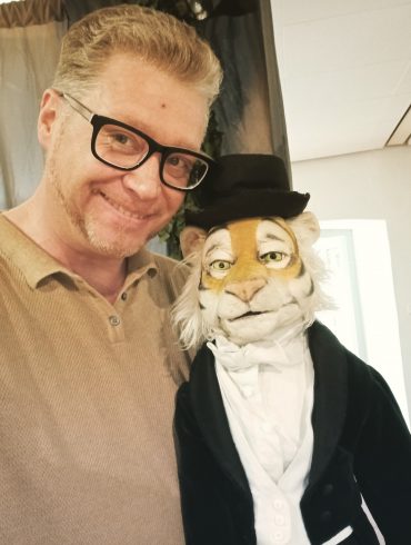 Der künstlerische Leiter des 29. Puppentheaterfests, Stefan Maatz, mit einer Tigerpuppe, die Frack und Zylinder trägt.
