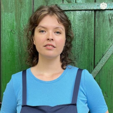 Die Organisatorische Mitarbeiterin der Astrid-Lindgren-Bühne Hannah Walther lehnt an einem grünen Scheunentor.